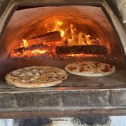  two pizzas cooking in a brick oven