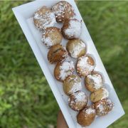 a person holding a box of powdered sugared donuts
