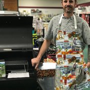 Dustin wearing a custom apron next to a Green Mountain Grill.