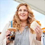 a woman holding two doughnuts and a drink