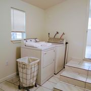 Dryer and washer in laundry room with a rolling laundry hamper.