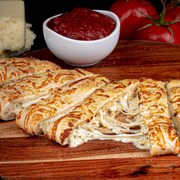 a wooden cutting board with a pizza cut in half and a bowl of tomato sauce in the background