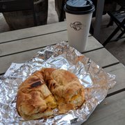 Breakfast sandwich on croissant with sausage and avocado. And a large black coffee.