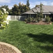 a lawn with a white fence and a house in the background