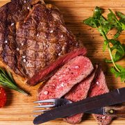 a steak on a cutting board with a knife and tomatoes